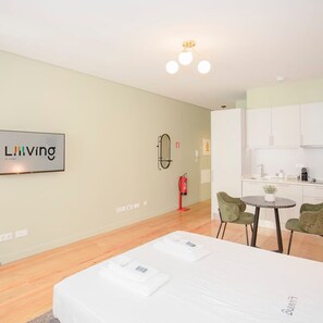 A modern hotel room with a bed, a small dining table, green chairs, a kitchen area, and a mounted TV displaying the word "Living". - Liiiving in Porto Historic Cl Rigos Studio - 2F (Porto)