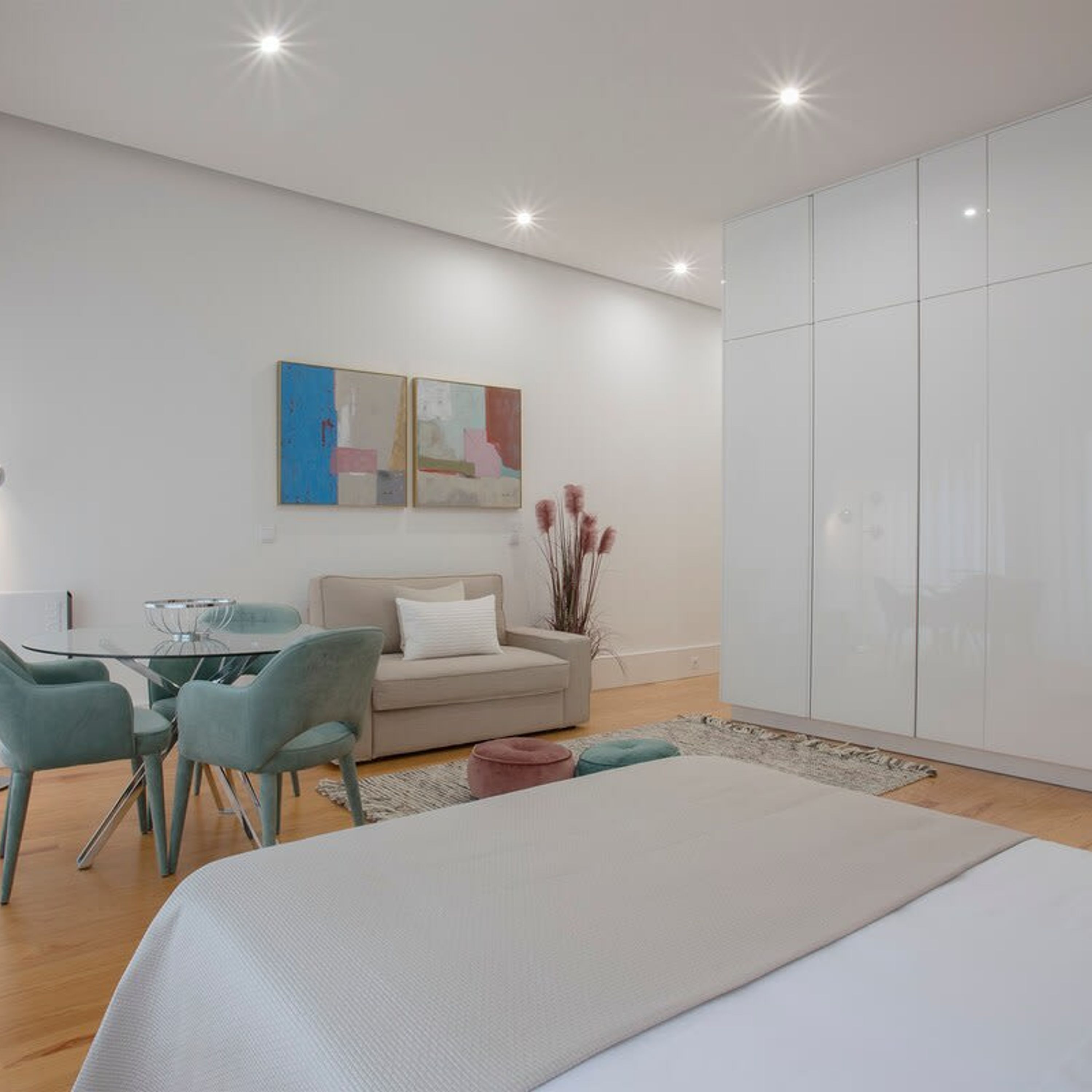A modern bedroom with a bed, a sofa, a dining table with chairs, and a large wardrobe.