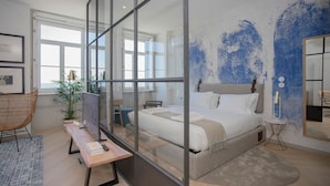Una camera da letto moderna con un letto grande, un divisorio in vetro, una scrivania, una sedia e un'ampia finestra.