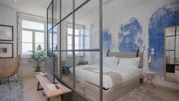 Quarto moderno com cama grande, divisória de vidro, escrivaninha, cadeira e janela ampla.