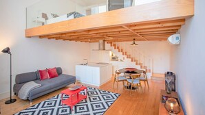 Ein modernes Loft mit Schlafgalerie, einer Küchenzeile, einem Essbereich und einem Wohnzimmer inklusive Sofa und Couchtisch.