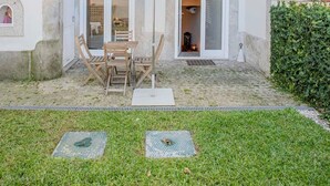 Eine Terrasse mit Tisch und Stühlen unter einem Sonnensegel, einer Hecke und einer Tür, die zu einem Raum führt.