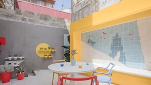A round table with chairs, a potted plant, and a wall with a tiled mural. - Liiiving in Porto - Cl Rigos Terrace Apartment (Porto)