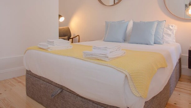 A neatly made bed with a yellow blanket, two pillows, and folded towels on a wooden floor. - Liiiving in Porto - Cl Rigos Terrace Apartment (Porto)