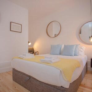 A neatly made bed with a yellow blanket, two pillows, and folded towels on a wooden floor. - Liiiving in Porto - Cl Rigos Terrace Apartment (Porto)