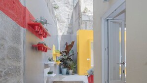 A narrow alleyway with a staircase leading to a yellow door, potted plants, and a red shelf. - Liiiving in Porto - Cl Rigos Terrace Apartment (Porto)