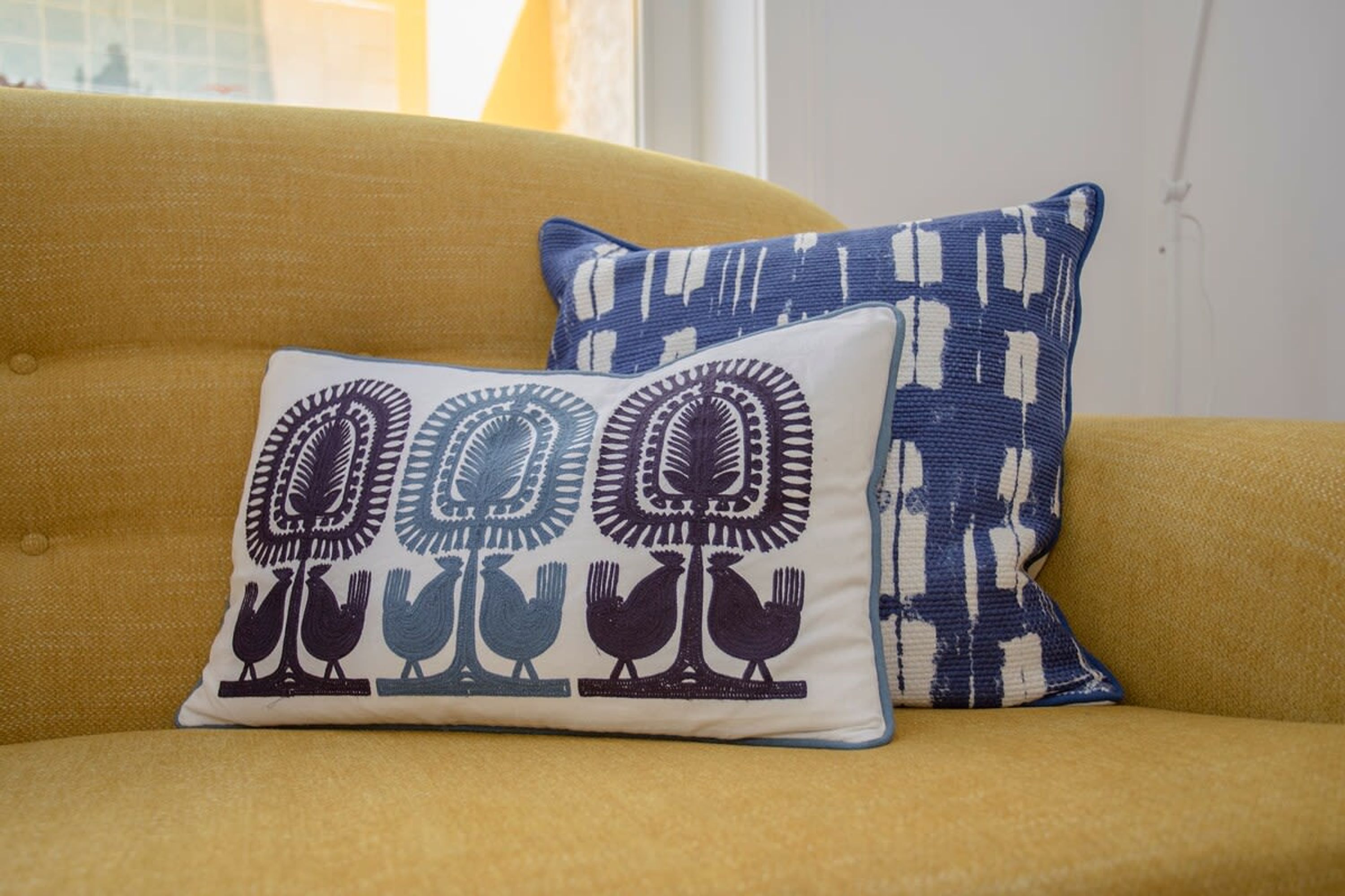 A yellow sofa with two decorative pillows, one featuring a bird pattern and the other a geometric design.