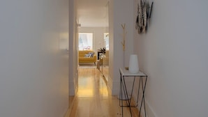 A hallway with wooden flooring, a yellow sofa, and a white table with decorative items. - Liiiving in Porto - Cl Rigos Terrace Apartment (Porto)