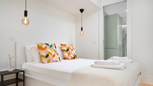 Une chambre moderne avec un grand lit, des coussins colorés, une table de chevet avec une lampe et un lit bien fait, agrémenté de serviettes.