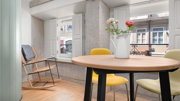 Un coin repas avec une table ronde, des chaises jaunes, un fauteuil en osier et un vase rempli de fleurs.