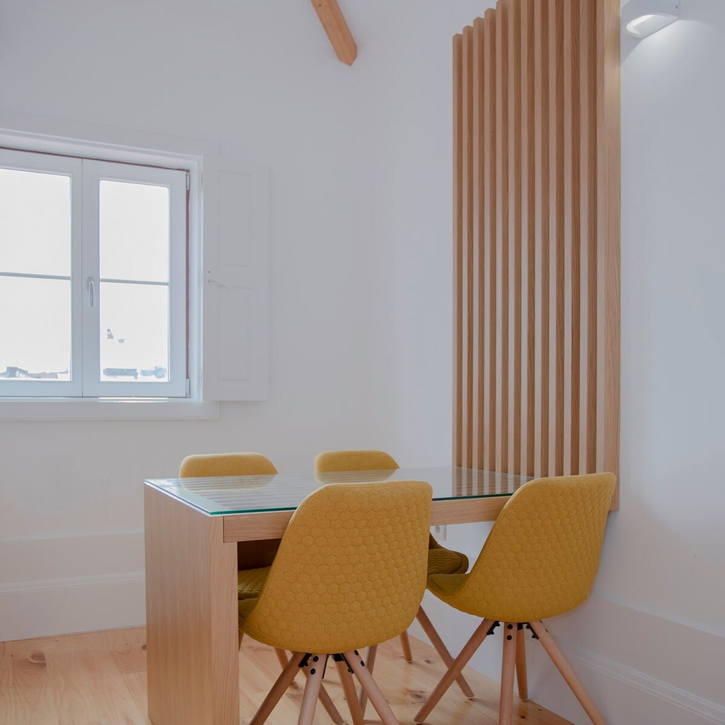 A dining area with a glass table, wooden chairs, and a vertical wooden panel.