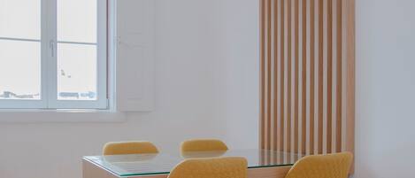 A dining area with a glass table, wooden chairs, and a vertical wooden panel.