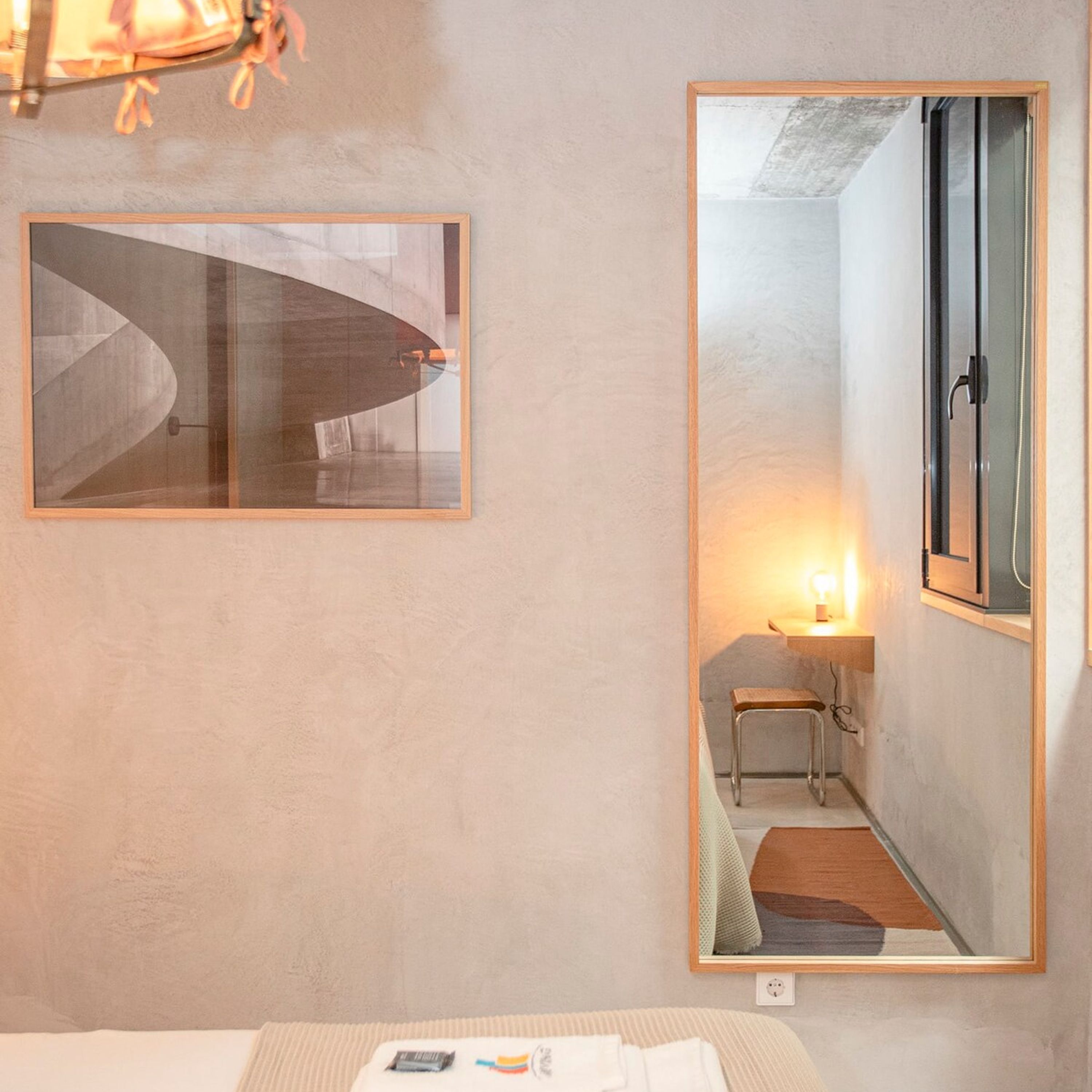 A hotel room with a bed, a bedside table, a mirror, and a framed picture on the wall.