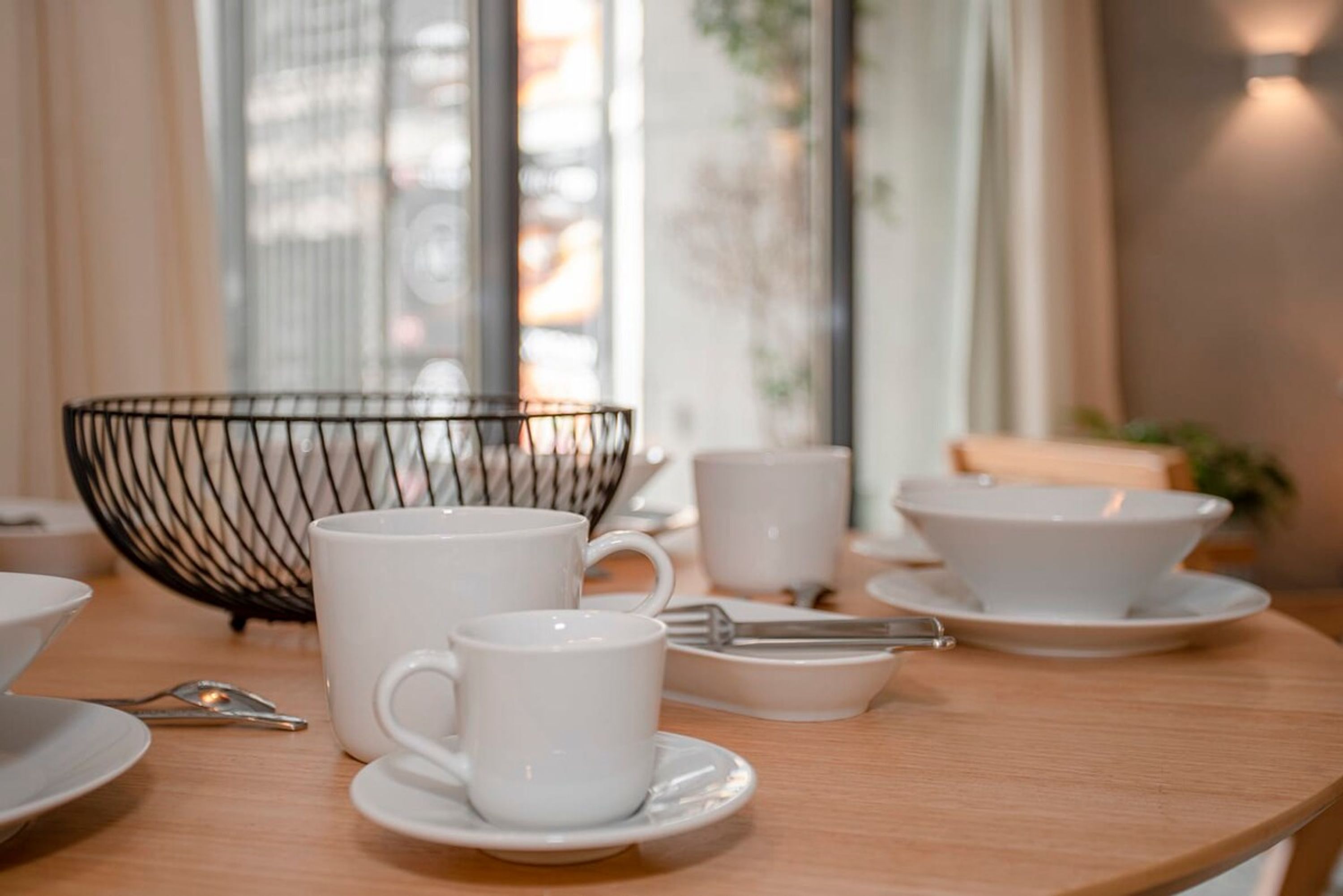 A dining table with white cups, saucers, and a metal bowl.