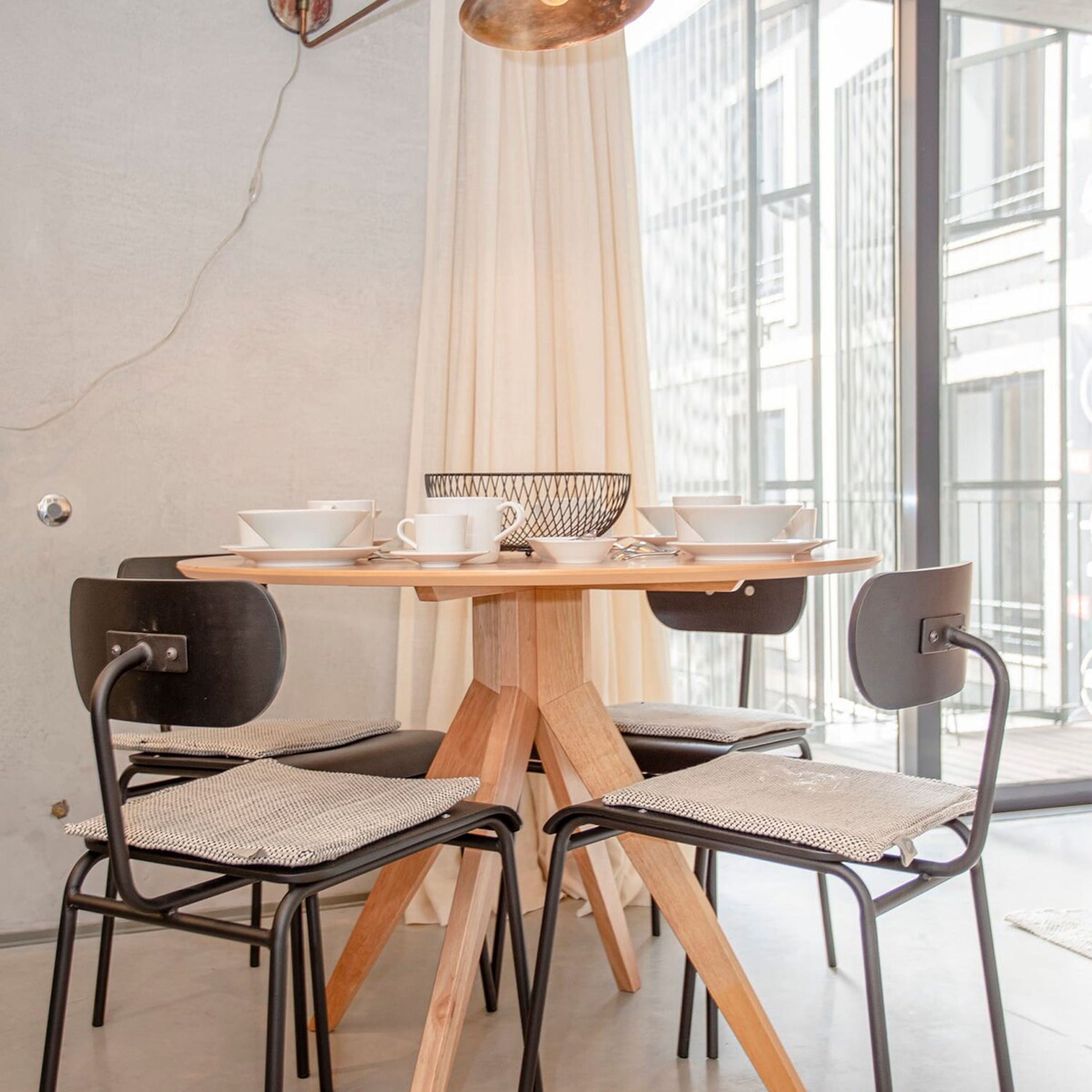 A dining area with a round wooden table, four chairs, and a black wire basket.