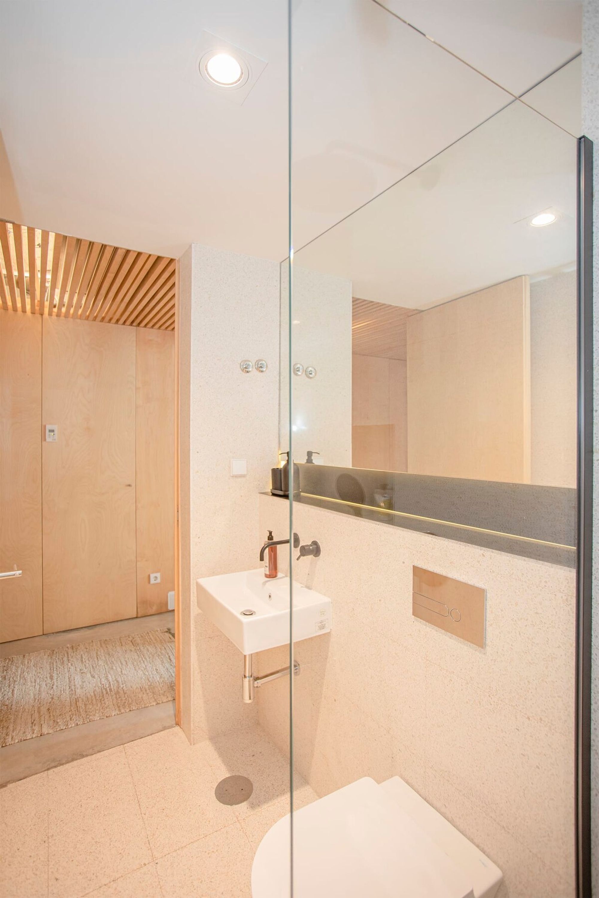 A modern bathroom with a glass partition, a wooden shower enclosure, a white sink, and a large mirror.