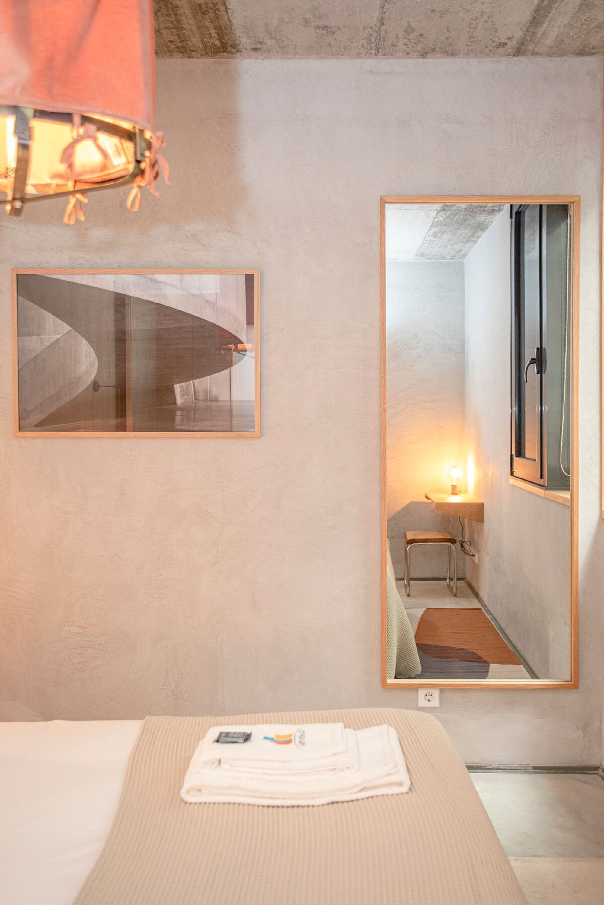 Une chambre d’hôtel avec un lit, un tableau encadré, un miroir et une table de chevet avec une lampe.
