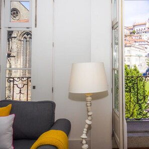 Ein Zimmer mit grauem Sofa, gelber Decke, weißer Lampe und Blick auf Gebäude durch ein Fenster.