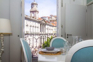 A dining area with a table set for two, overlooking a cityscape with a prominent clock tower. - Liiiving in Porto Ribeira Boutique Apartment (Porto)