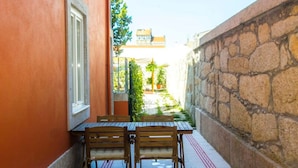 A narrow outdoor corridor with a table and chairs, a stone wall on one side, and a building in the background. - Liiiving in Porto Central Garden Flat (Porto)