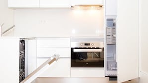 A compact kitchen with white cabinetry, a built-in oven, and a dishwasher. - Liiiving in Porto Central Garden Flat (Porto)
