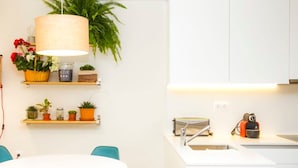 A modern kitchen with white cabinets, a white countertop, and a sink. There is a round table with teal chairs and a white tablecloth. - Liiiving in Porto Central Garden Flat (Porto)