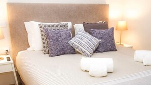A neatly made bed with striped bedding and multiple pillows, a bedside table with a lamp, and a wooden floor. - Liiiving in Porto Central Garden Flat (Porto)