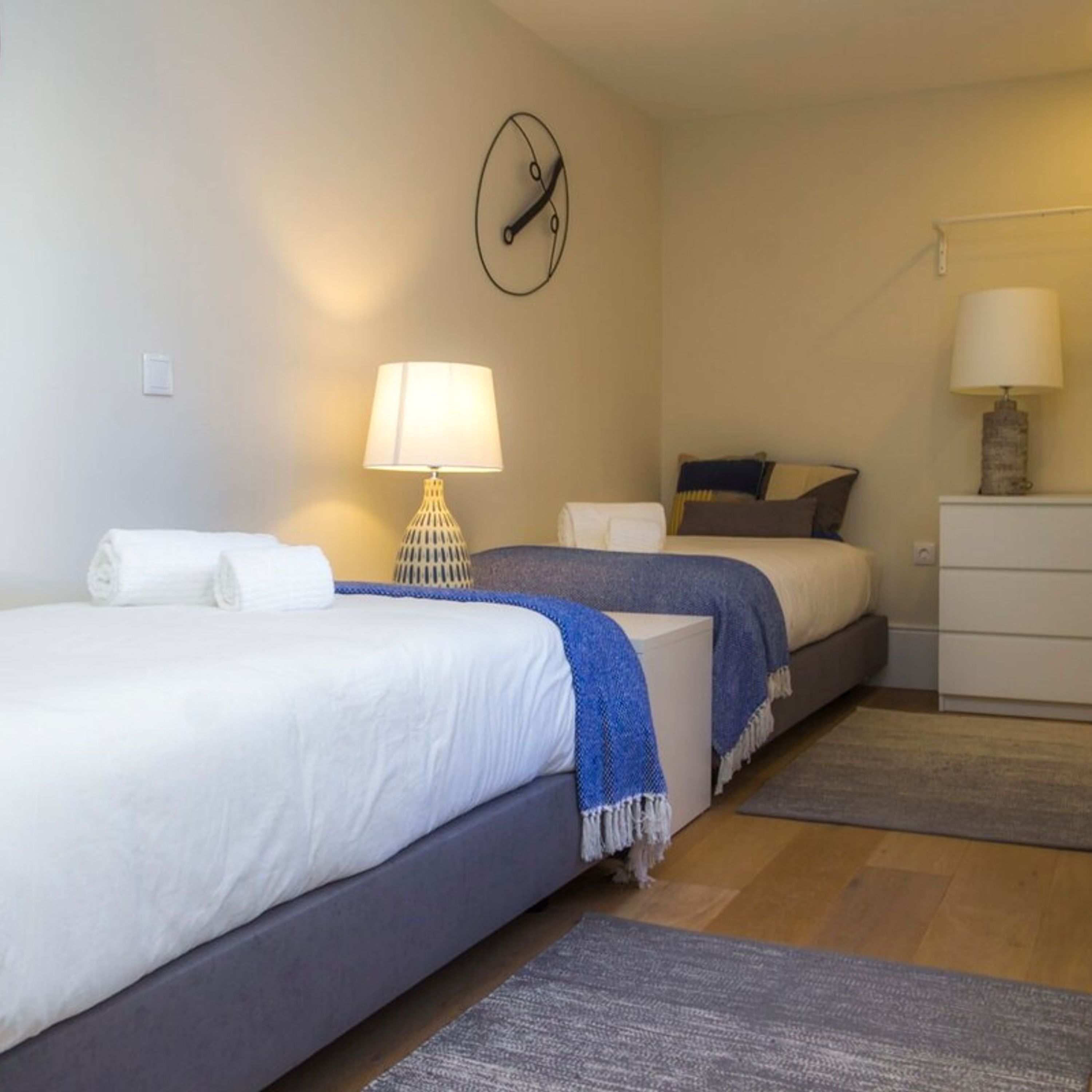 Ein Hotelzimmer mit zwei Betten, einer Wanduhr, einer Lampe und einem Schminktisch.