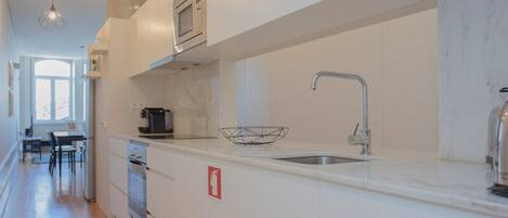 A modern kitchen with white cabinetry, a stainless steel sink, and a microwave. There are emergency signs on the wall and a fire extinguisher on the counter.