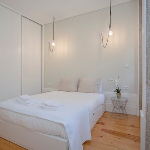 Un dormitorio moderno con una cama bien hecha, una mesita redonda con una planta y dos lámparas colgantes.