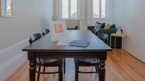 Ein modernes Wohnzimmer mit Esstisch, zwei Stühlen, einem grünen Sofa und einem kleinen Beistelltisch.