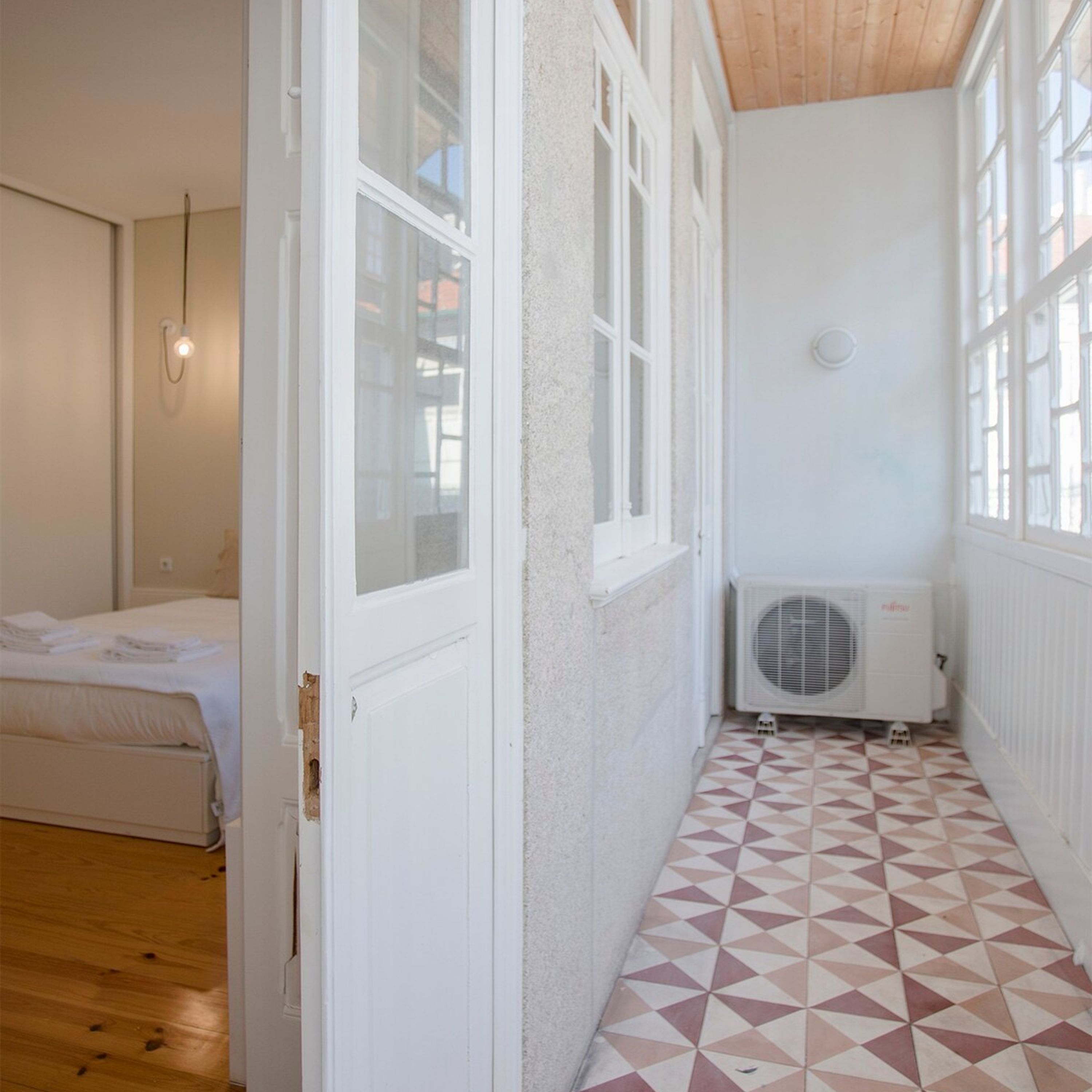 A narrow hallway with a patterned floor, a bed with neatly made sheets, and a white radiator.