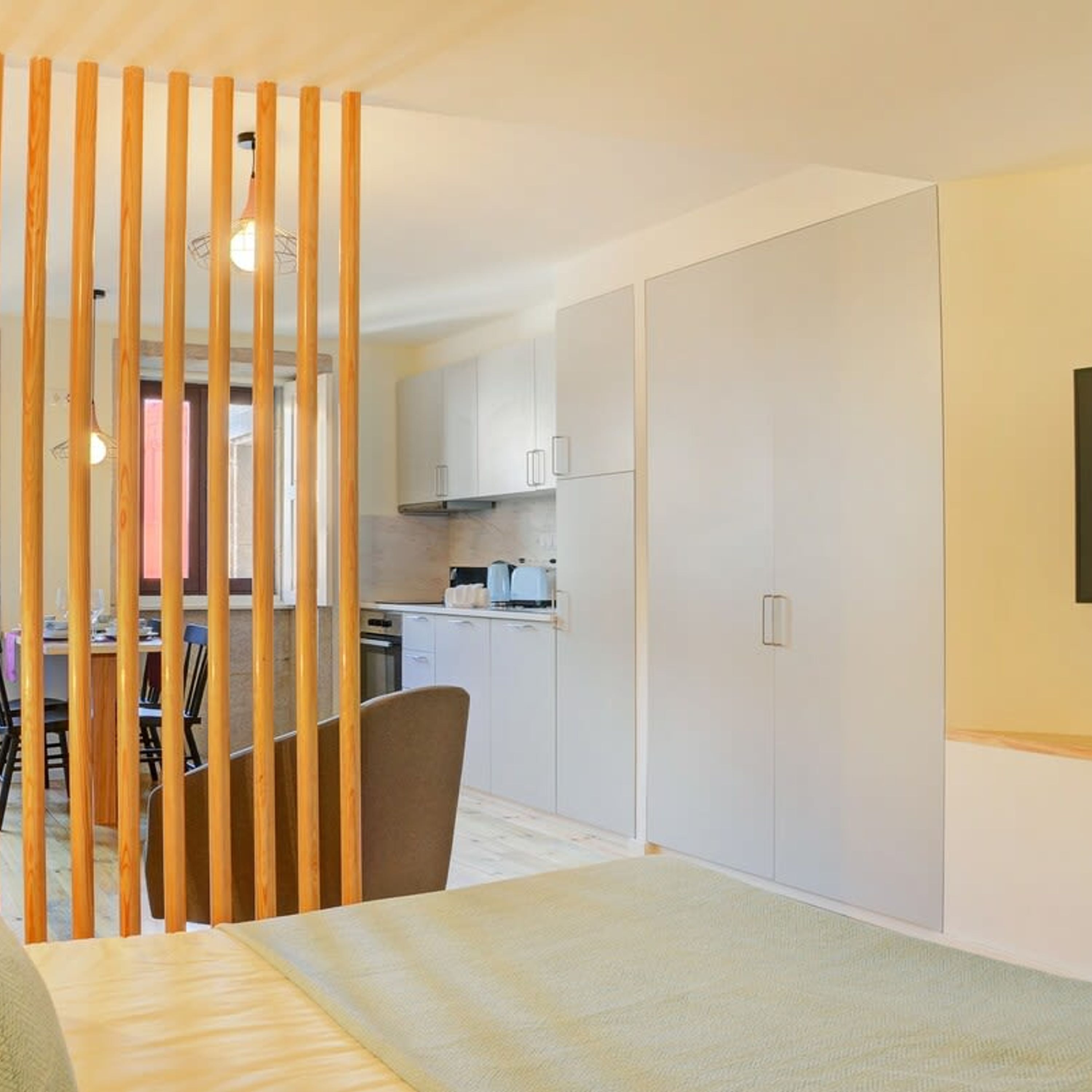 Eine moderne Küche mit weißen Schränken, ein Essbereich mit Tisch und Stühlen sowie eine Holzwand.