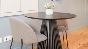 A modern room with a round table, two chairs, a potted plant, a wall-mounted mirror, and a fire alarm. - Liiiving in Porto Historic Cl Rigos Studio - 1F (Porto)