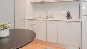A modern kitchen with white cabinets, a dark wooden table, and a small potted plant. - Liiiving in Porto Historic Cl Rigos Studio - 1F (Porto)