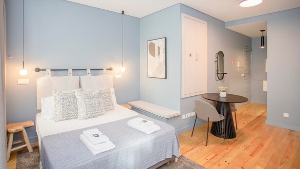 A modern bedroom with a bed, bedside table, and a small dining area with a table and chairs. - Liiiving in Porto Historic Cl Rigos Studio - 1F (Porto)