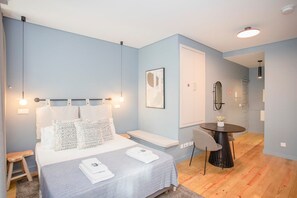 A modern bedroom with a bed, bedside table, and a small dining area with a table and chairs. - Liiiving in Porto Historic Cl Rigos Studio - 1F (Porto)