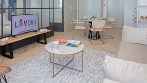 A modern living room with a television, seating, a dining area, and a large glass wall. - Liiiving in Porto Luxury Beachfront Apartment II (Porto)