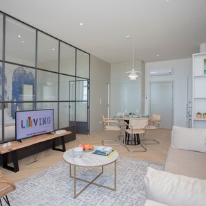A modern living room with a television, seating, a dining area, and a large glass wall. - Liiiving in Porto Luxury Beachfront Apartment II (Porto)