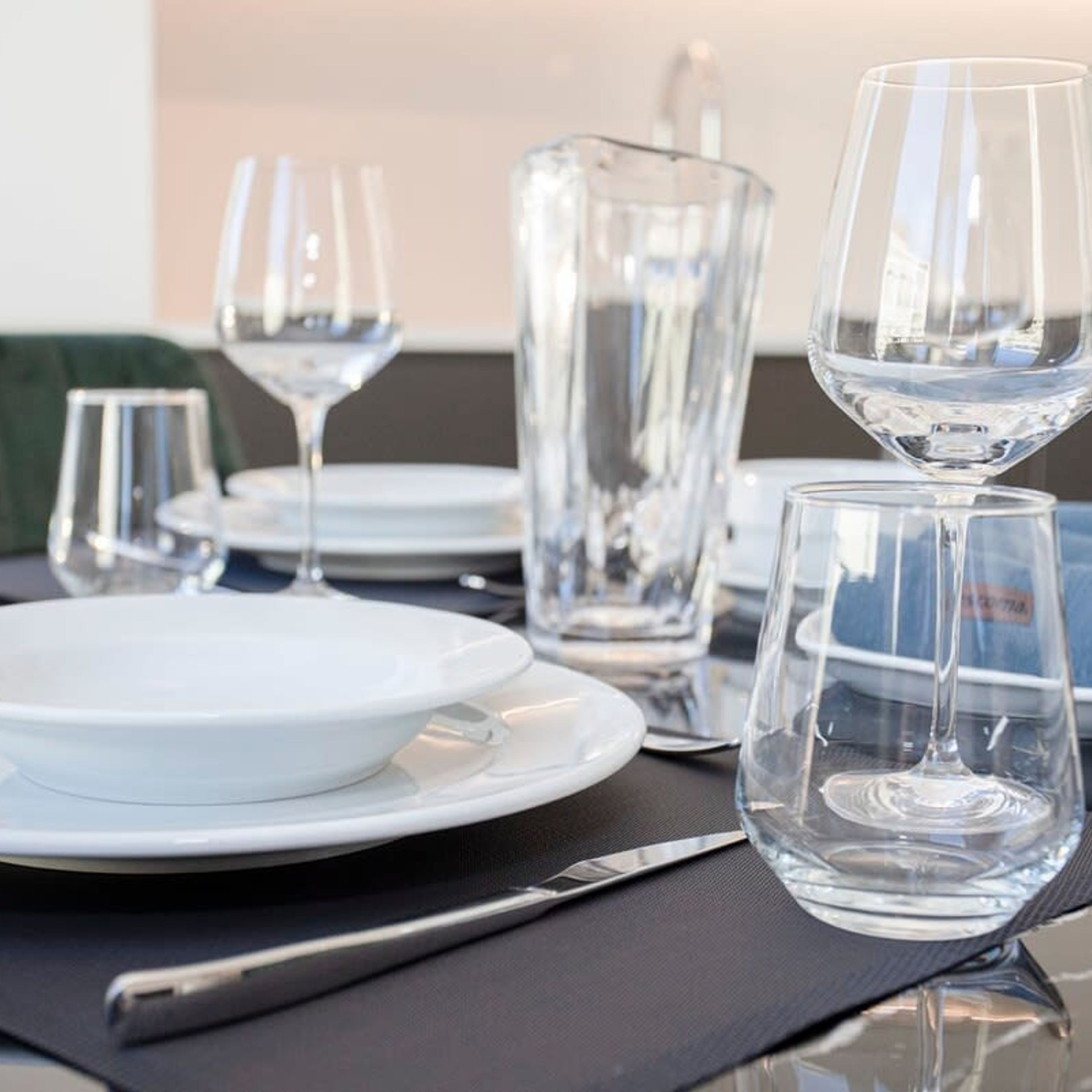 A table set with clear glassware and white plates, with a pitcher and a knife on the table.