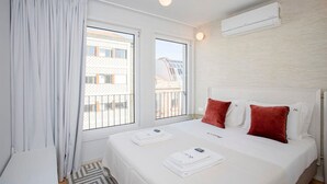 A hotel room with a bed, white curtains, two windows, a ceiling light fixture, and an air conditioning unit. - Liiiving in Porto-modern Glam Rooftop Apartment (Porto)