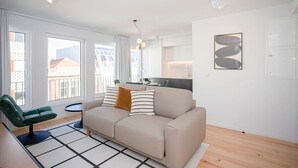 A modern living room with a sofa, a green armchair, and a dining area with a table and chairs. - Liiiving in Porto-modern Glam Rooftop Apartment (Porto)
