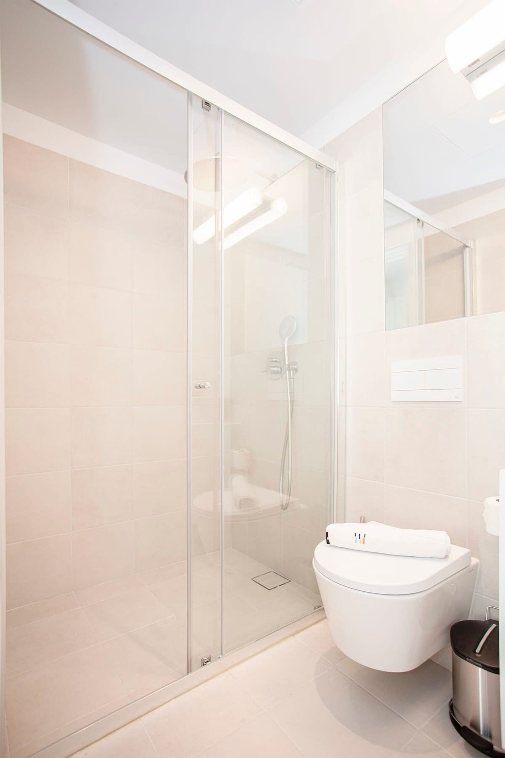 A modern bathroom with a glass shower enclosure, a white toilet, and a trash bin.