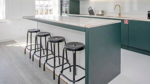 A modern kitchen with a central island, bar stools, and a window providing natural light. - Liiiving in Porto - Ribeira Riverside Apartment (Porto)