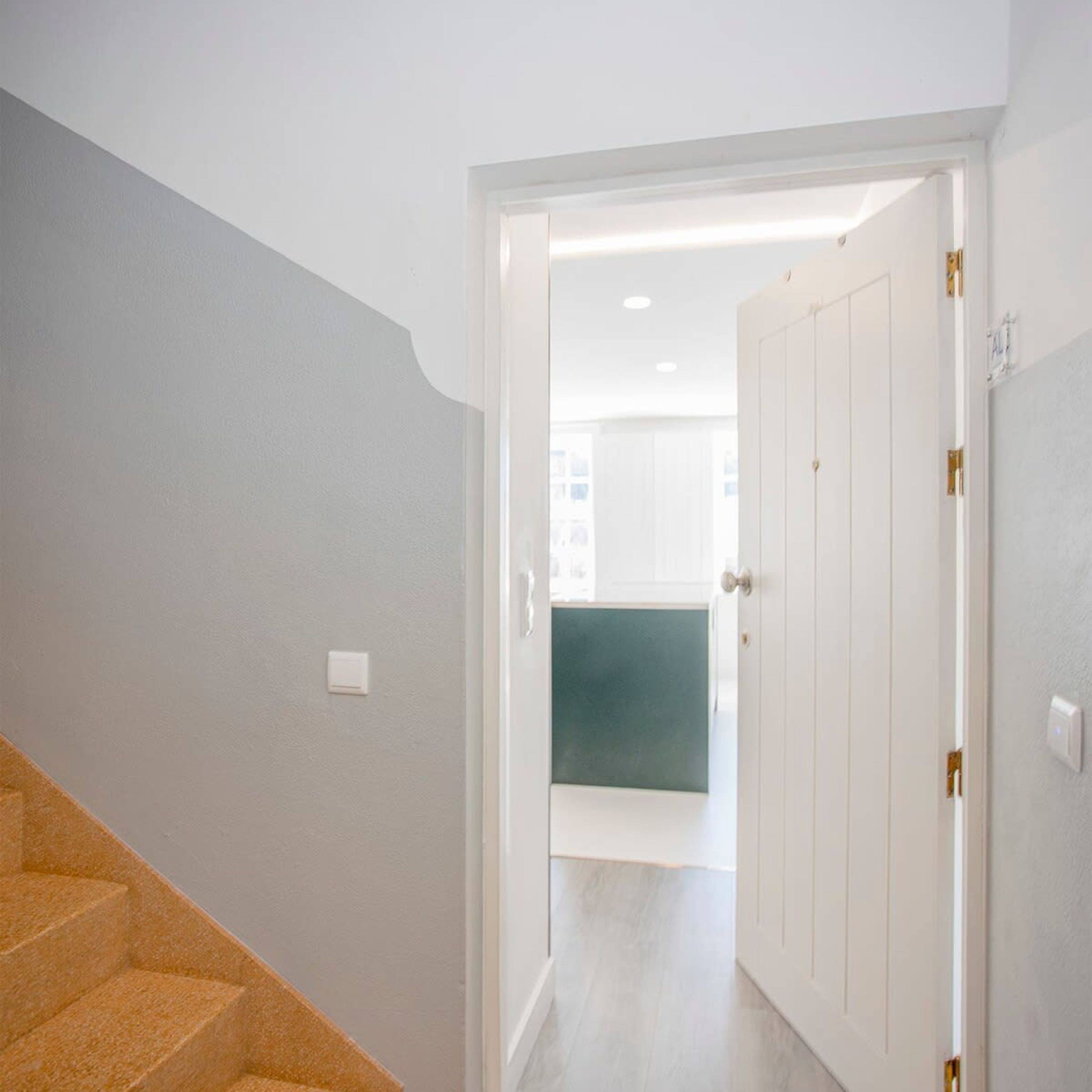 A hallway with a white door leading to a room with a green accent wall.