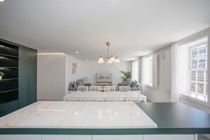 Une cuisine moderne dotée d’un plan de travail en marbre, de meubles blancs et d’un coin repas avec une table et des chaises blanches.