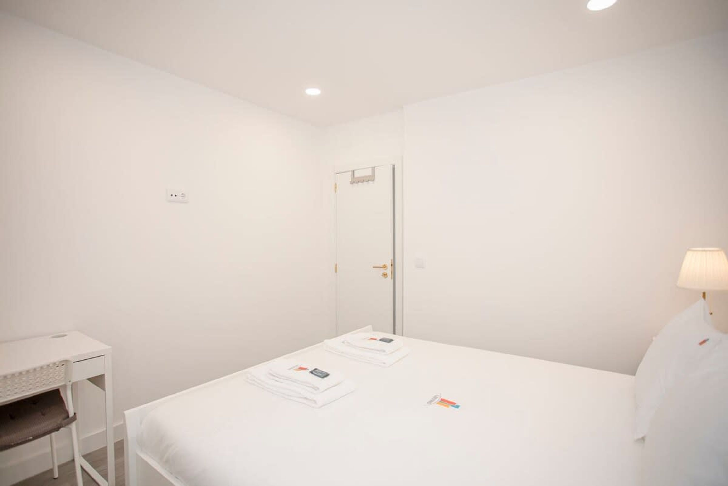 A white room with a bed, a desk, and a door.