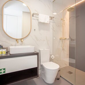 Une salle de bain moderne avec un grand miroir rond, un lavabo blanc, des toilettes et une douche à parois de verre.
