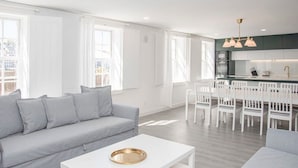 A modern living room with a grey sofa, a white coffee table with a gold tray, and a kitchen area with white cabinets and a dining set. - Liiiving in Porto - Ribeira Riverside Apartment (Porto)
