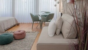 A modern bedroom with a bed, a sofa, a dining table with chairs, and a large window with sheer curtains. - Liiiving in Porto Downtown Luxury Apartment 1R (Porto)
